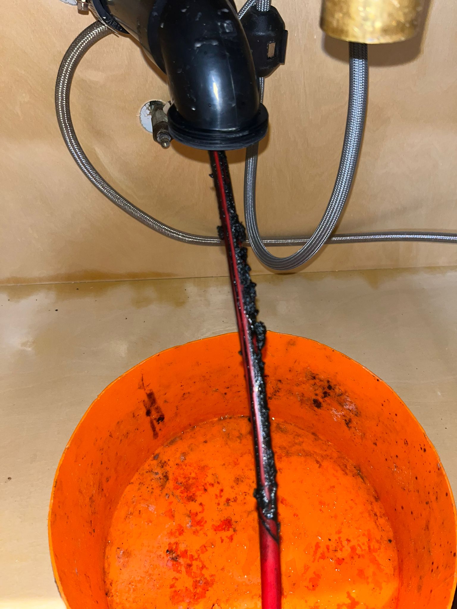Pipe resurfacing cable feeding into drain line with orange catch bucket, drain cleaning in Maple Ridge