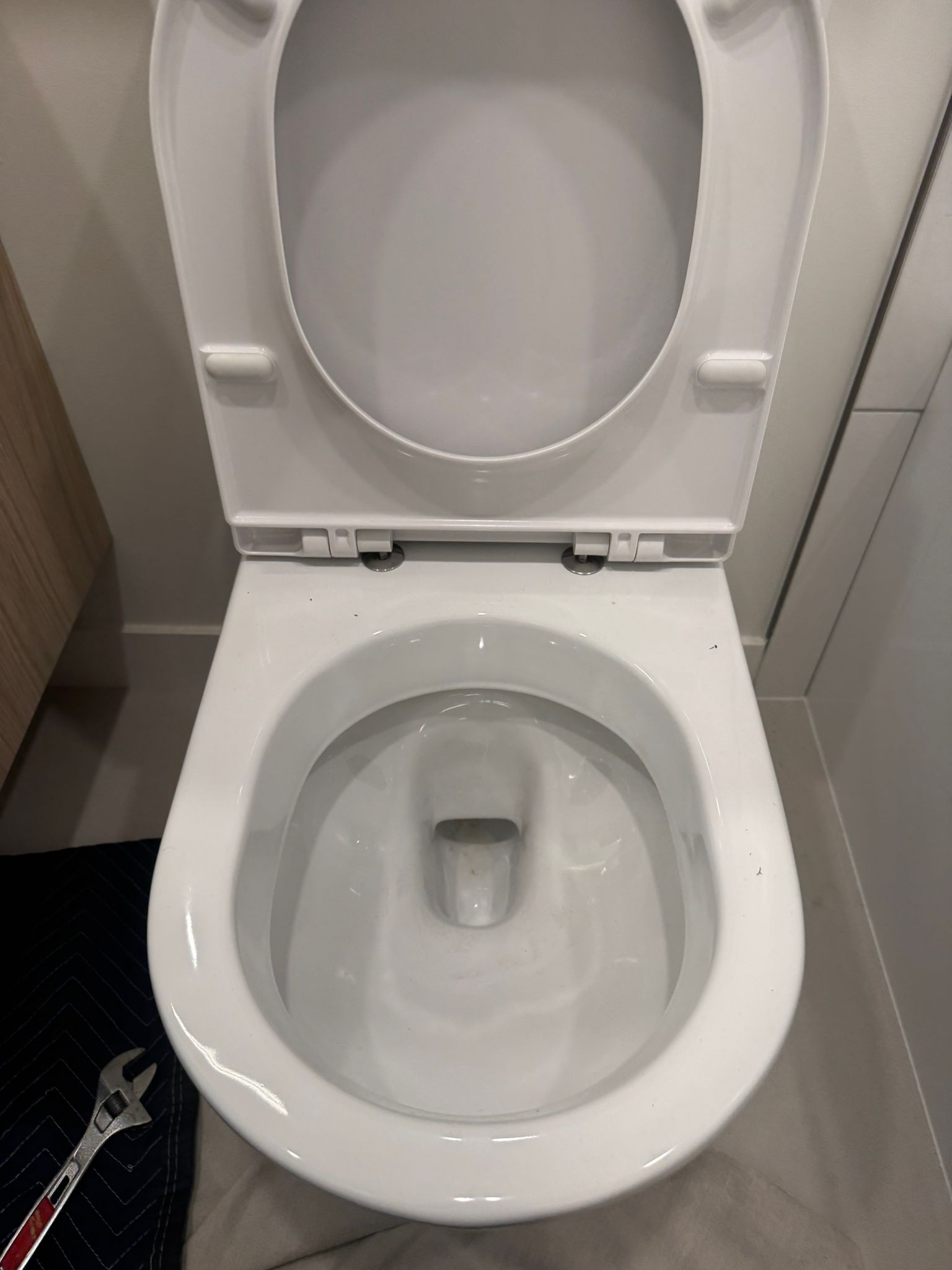 Reinstalled white toilet bowl with open seat in tiled washroom, drain cleaning in Coquitlam