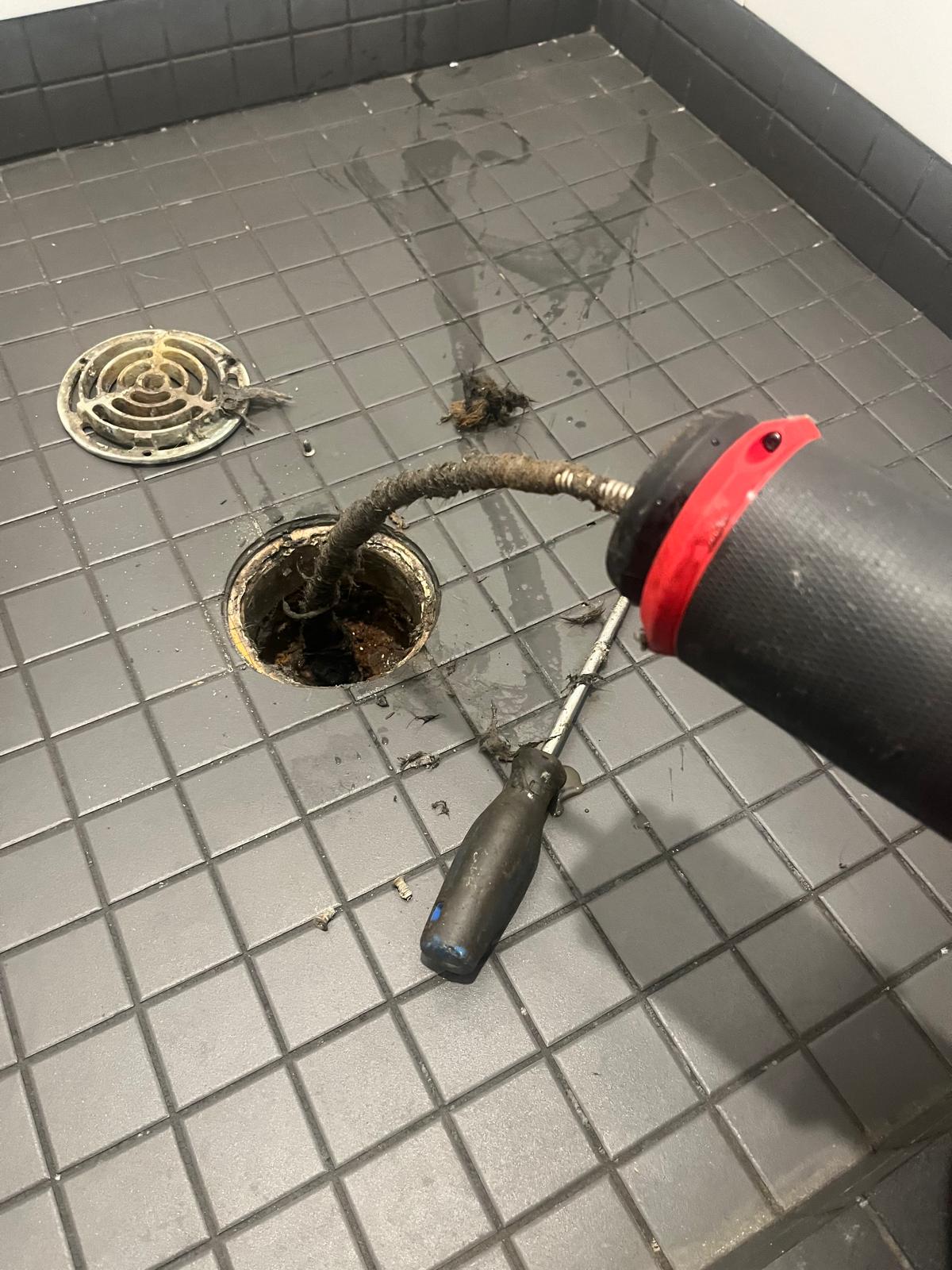 Small powered drain snake fed into tiled shower drain opening, commercial plumbing in Coquitlam