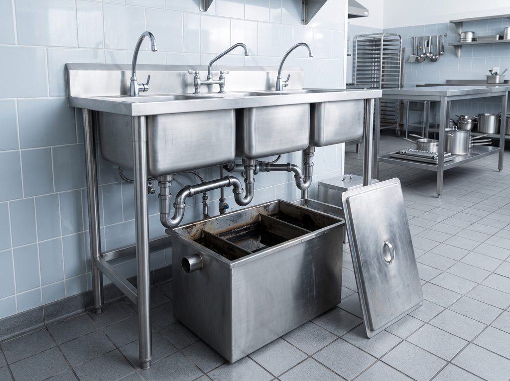 Floor-mounted grease interceptor under a restaurant kitchen sink with the lid removed